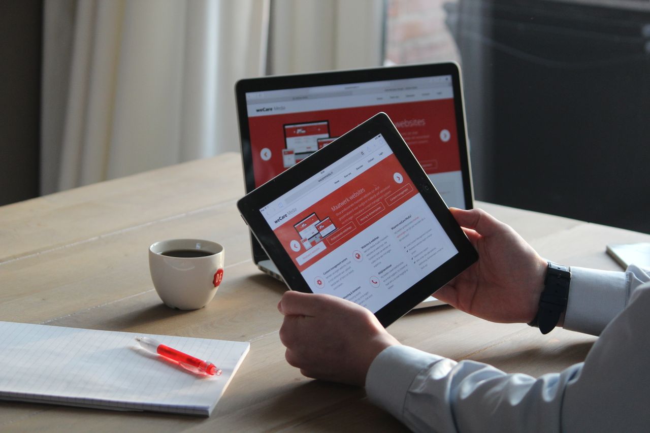 creative Business professional using a tablet and laptop with a hot drink, focusing on digital content review.
